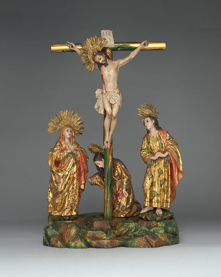 A green stand that holds three figures side by side crafted in polychrome wood.